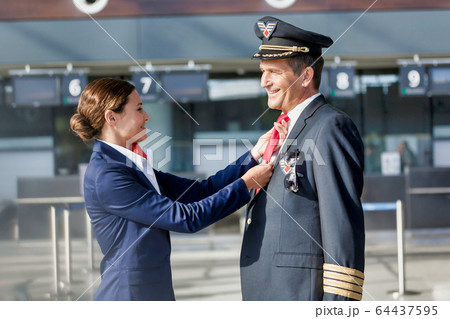 Young attractive flight attendant adjusting pilot Young attractive flight attendant adjusting pilot 64437595