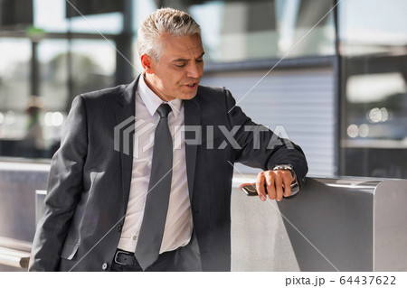 Mature businessman checking time on his wristwatch Mature businessman checking time on his wristwatch 64437622