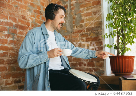 Caucasian musician playing hand drum during online concert at home isolated and quarantined, greeting band and coffee drinking 64437952