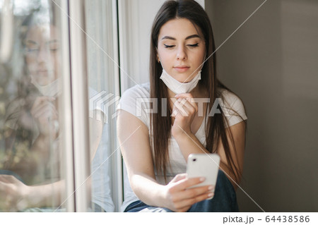 Young Woman take off protective mask and use smartphone. End of quarantine. Coronavirus theme 64438586