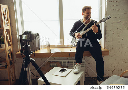 Caucasian musician playing guitar during online concert at home isolated and quarantined, cheerful improvising Caucasian musician playing guitar during online concert at home isolated and quarantined, cheerful improvising 64439236