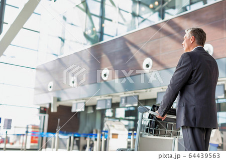 Mature businessman pushing baggage cart for check Mature businessman pushing baggage cart for check 64439563