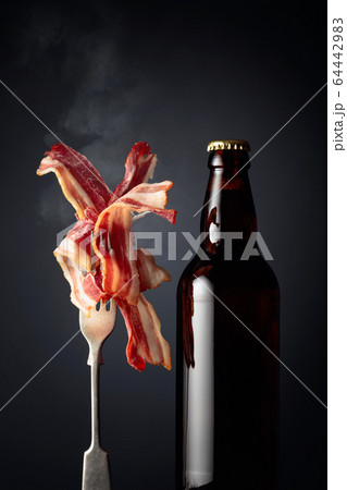 Slices of tasty fried bacon and beer bottle. 64442983