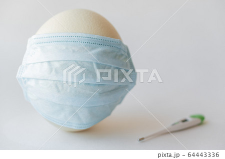 Large white easter ostrich egg in a medical mask and a thermometer. Egg in a respirator and a thermometer. Easter and Coronavirus, Covid-19. Ostrich egg in a medical mask and a thermometer on a white Large white easter ostrich egg in a medical mask and a thermometer. Egg in a respirator and a thermometer. Easter and Coronavirus, Covid-19. Ostrich egg in a medical mask and a thermometer on a white 64443336