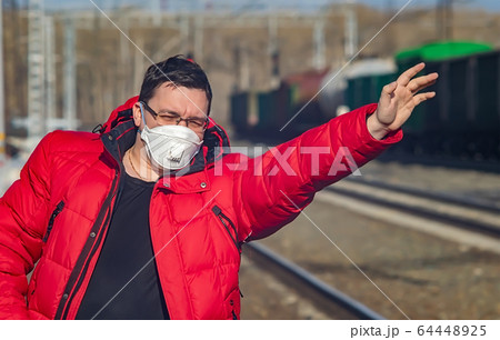 a man in a medical mask waves to the train 64448925