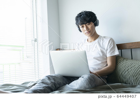 ヘッドホンをしてパソコンを操作する若い男性 64449407