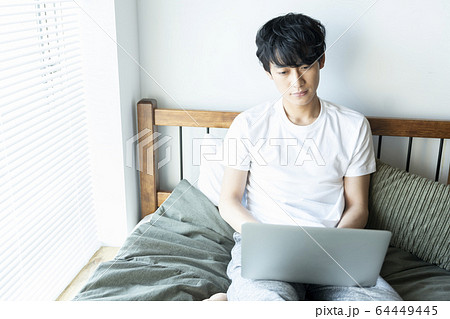 ベッドに座ってパソコンを操作する若い男性　20代の男性　ライフスタイル 64449445