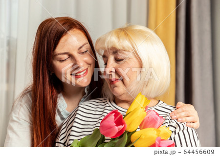 Mother and young daughter are hugging. Happy loving family.Blonde 50 year woman holding a fresh beautiful bouquet of flowers. Happy relationship Mother and young daughter are hugging. Happy loving family.Blonde 50 year woman holding a fresh beautiful bouquet of flowers. Happy relationship 64456609