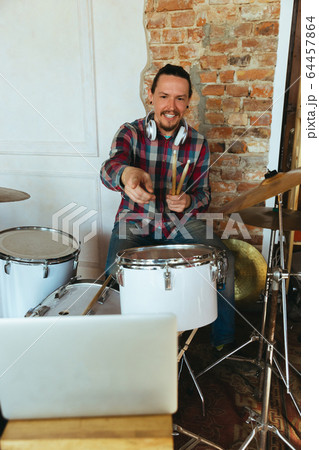 Caucasian musician playing drumms during online concert with the band at home isolated and quarantined, greeting audience Caucasian musician playing drumms during online concert with the band at home isolated and quarantined, greeting audience 64457864