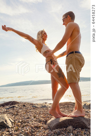 Happy and Smiling Young Couple Standing On Rock At Beach 64458273