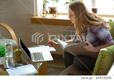 Young woman studying at home during online courses or free information by herself, making notes Young woman studying at home during online courses or free information by herself, making notes 64459999