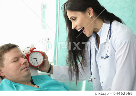 Nurse holds an alarm clock near patients face 64462969