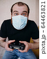 Adult balding white man playing video games with medical mask on his face while Covid-19 quarantine 64463821