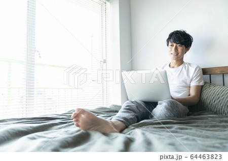 ベッドに座ってパソコンを操作する若い男性 ベッドに座ってパソコンを操作する若い男性 64463823