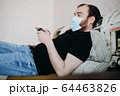 Adult balding white man playing video games with medical mask on his face while Covid-19 quarantine 64463826