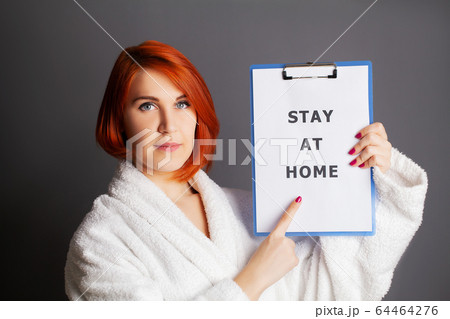 Woman holding blank with inscription stay at home calling for stop spreading covid-19 64464276
