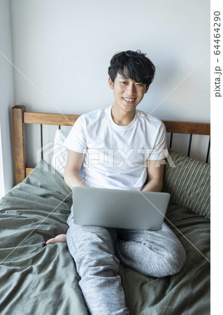 ベッドに座ってパソコンを操作する若い男性　20代の男性　ライフスタイル　イメージ 64464290