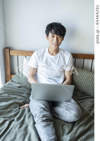 ベッドに座ってパソコンを操作する若い男性 20代の男性 ライフスタイル イメージ ベッドに座ってパソコンを操作する若い男性 20代の男性 ライフスタイル イメージ 64464291