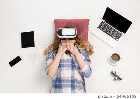 Emotional caucasian woman using VR-headsed, surrounded by gadgets isolated on white studio background, technologies. Shocked, scared 64466108