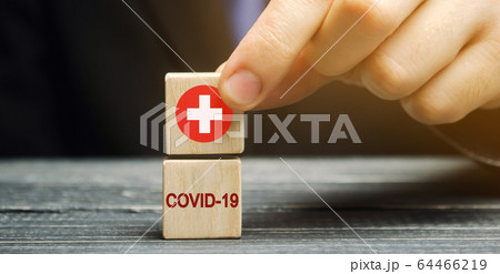 A man holds a block with a medical cross and the inscription Covid-19. Coronavirus pandemic infection. Healthcare, medicine concept. Health insurance. Ambulance. Quarantine, lockdown 64466219