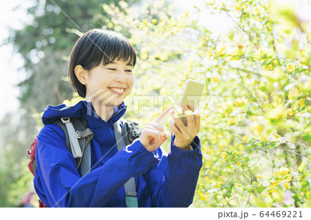 ハイキング中スマホで植物を撮る女性 64469221