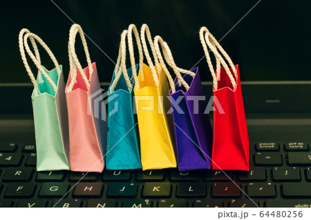 Row colorful paper shopping bags with mobile phone on a laptop keyboard. Ideas about online shopping or shopping at home or office which customers can purchase items or services or goods remotely. Row colorful paper shopping bags with mobile phone on a laptop keyboard. Ideas about online shopping or shopping at home or office which customers can purchase items or services or goods remotely. 64480256