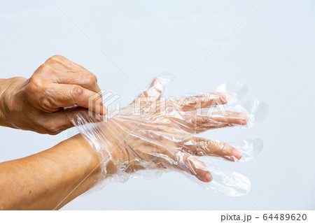 Senior woman's hands wearing disposable protective plastic glove on grey background, Close up shot, Prevention from covid19, Coronavirus, Bacteria, Healthcare 64489620