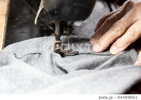 Senior woman's stitching grey fabric on vintage sewing machine, Thread, Needle, Close up shot, Selective focus, Sewing process, Female's hobby. Tailor concept 64489661