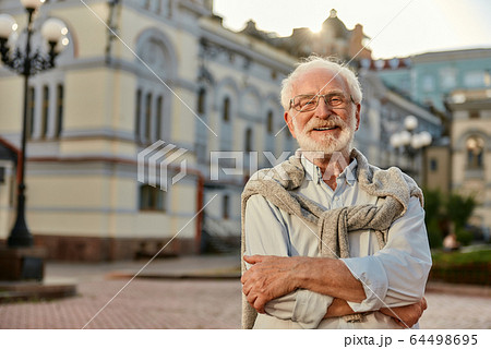 Always in good mood. Portrait of handsome bearded senior man in glasses looking at camera and smiling while standing outdoors Always in good mood. Portrait of handsome bearded senior man in glasses looking at camera and smiling while standing outdoors 64498695