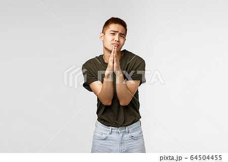 Clingy taiwanese teenage guy begging parents let him go party, shaking pleading hands, clasp arms together in pray and frowning, asking help, appologizing, standing grey background 64504455