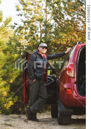 Man in tourist clothes in forest near car. Man in tourist clothes in forest near car. 64504601