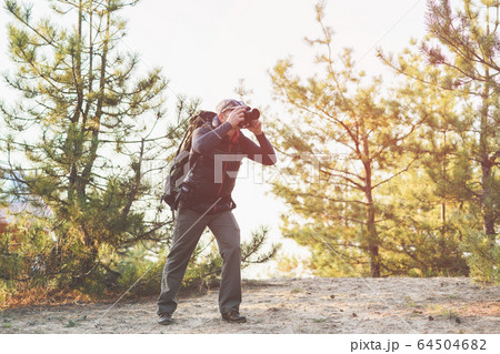 Senior man taking photo by camera in forest Senior man taking photo by camera in forest 64504682