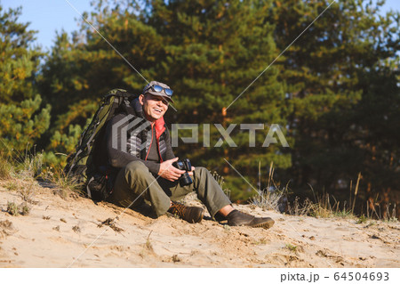 Smiing tourist sit with camera and backpack 64504693