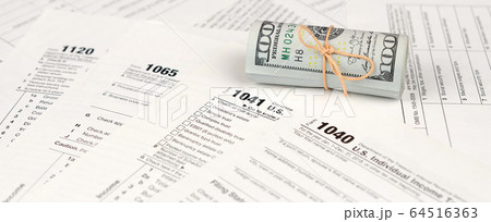 Tax forms lies near roll of hundred dollar bills. Tax forms lies near roll of hundred dollar bills. 64516363