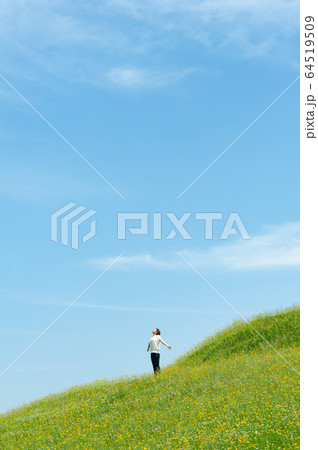 黄色い花咲く草原で深呼吸をする女性 64519509