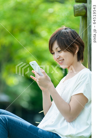 木陰でスマホを見る女性 64519543
