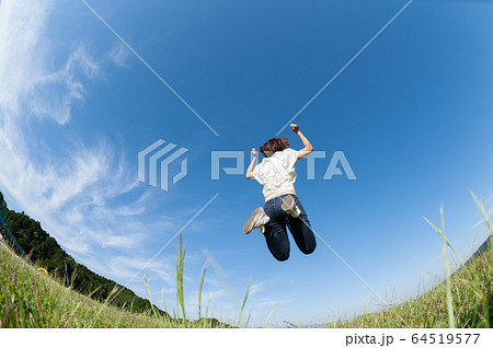 草原でジャンプする女性の後ろ姿の写真素材