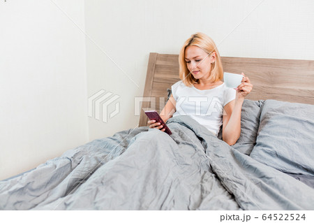 Beautiful young woman using phone in bed Beautiful young woman using phone in bed 64522524