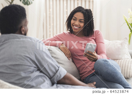 Young african couple chatting at home, relaxing on sofa together 64523874