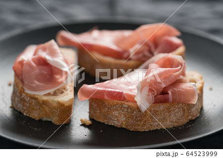 ciabatta with thin prosciutto on black plate on linen background ciabatta with thin prosciutto on black plate on linen background 64523999