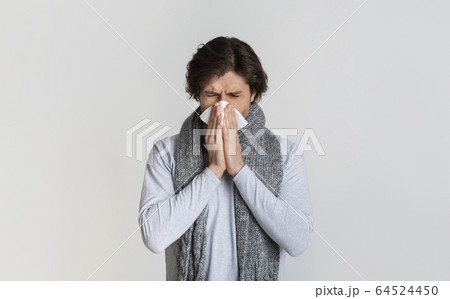 Man with scarf, blows nose in napkin 64524450