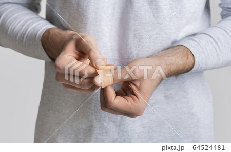 Man wrapping wound on finger with band-aid 64524481
