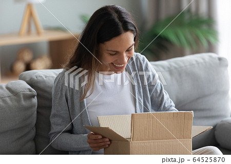 Smiling young woman unpacking parcel, opening cardboard box 64525870