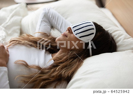 Close up sincere woman wearing sleeping mask resting in bed 64525942