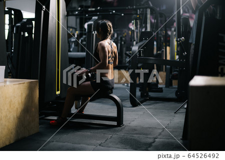 Fitness young woman with perfect athletic body wearing black sportswear sitting at simulator. Fitness young woman with perfect athletic body wearing black sportswear sitting at simulator. 64526492