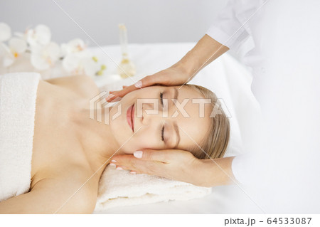 Beautiful caucasian woman enjoying facial massage with closed eyes in spa salon. Relaxing treatment in medicine and Beauty concept 64533087