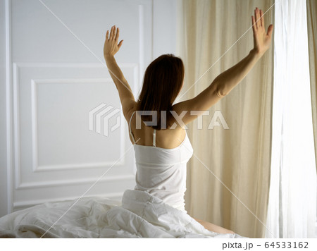 Woman stretching in bed after waking up, back view, entering a day happy and relaxed after good night sleep. Good morning and new day for brunette. Concept of Weekend, holidays 64533162