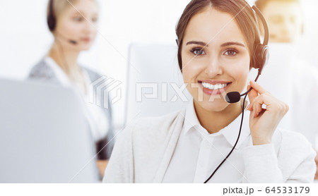 Call center in sunny office. Group of diverse operators at work. Beautiful woman in headset communicating with customers of telemarketing service. Business concept 64533179