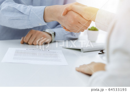 Casual dressed businessman and woman shaking hands after contract signing in sunny office. Handshake concept Casual dressed businessman and woman shaking hands after contract signing in sunny office. Handshake concept 64533193