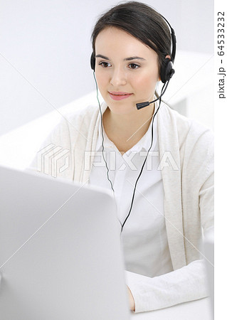 Call center. Casual dressed woman working in headset with diverse colleagues at office. Business concept Call center. Casual dressed woman working in headset with diverse colleagues at office. Business concept 64533232